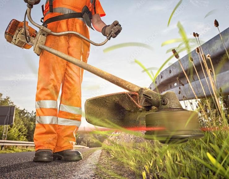 Straßenwärter beim Mähen Straßenwärter in Warnkleidung mäht Gras am Straßenrand